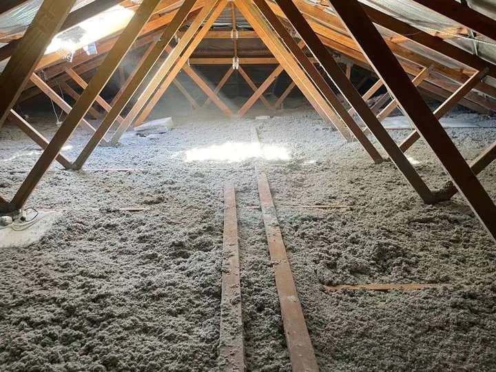 Grey cellulose insulation across a wide timber-framed roof space.