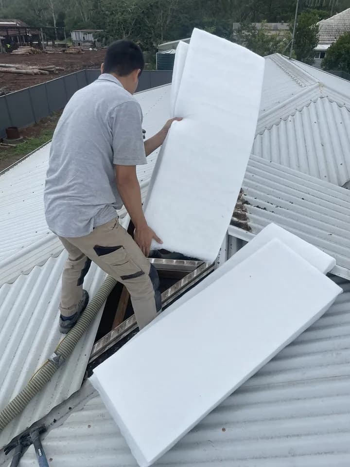 Installer feeding white polyester batts through an opened roof section.